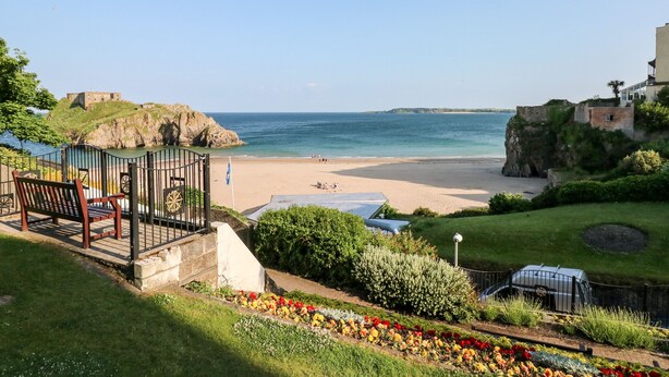 A coastal view with a beach, a historic building, and a garden with colorful flowers. - Clicketts Court (Tenby)