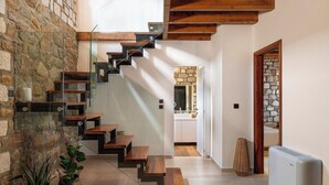 Una escalera con peldaños de madera y barandillas de vidrio que conduce a una cocina con paredes de piedra y un diseño moderno.