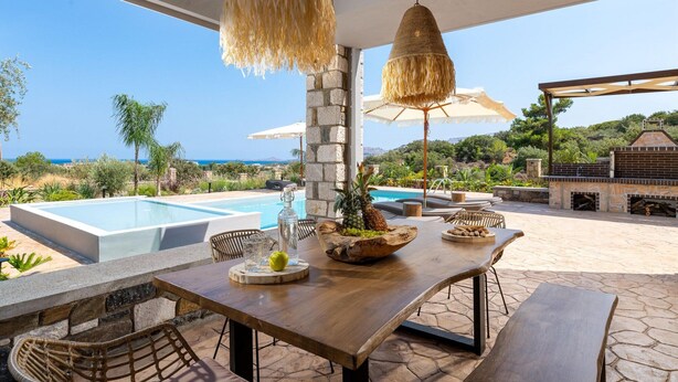 Un área de comedor al aire libre con piscina, una parrilla y vistas al mar.