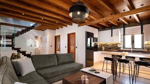 Un interior moderno con techo de madera, un sofá verde, una mesa de centro, una zona de cocina y una escalera.