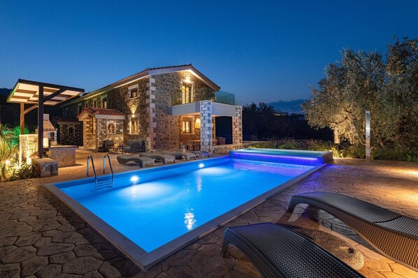 A modern outdoor pool area with stone walls, lounge chairs, and a well-lit patio.