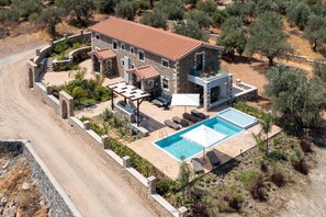 A two-story stone house with a swimming pool, outdoor seating, and a stone pathway.