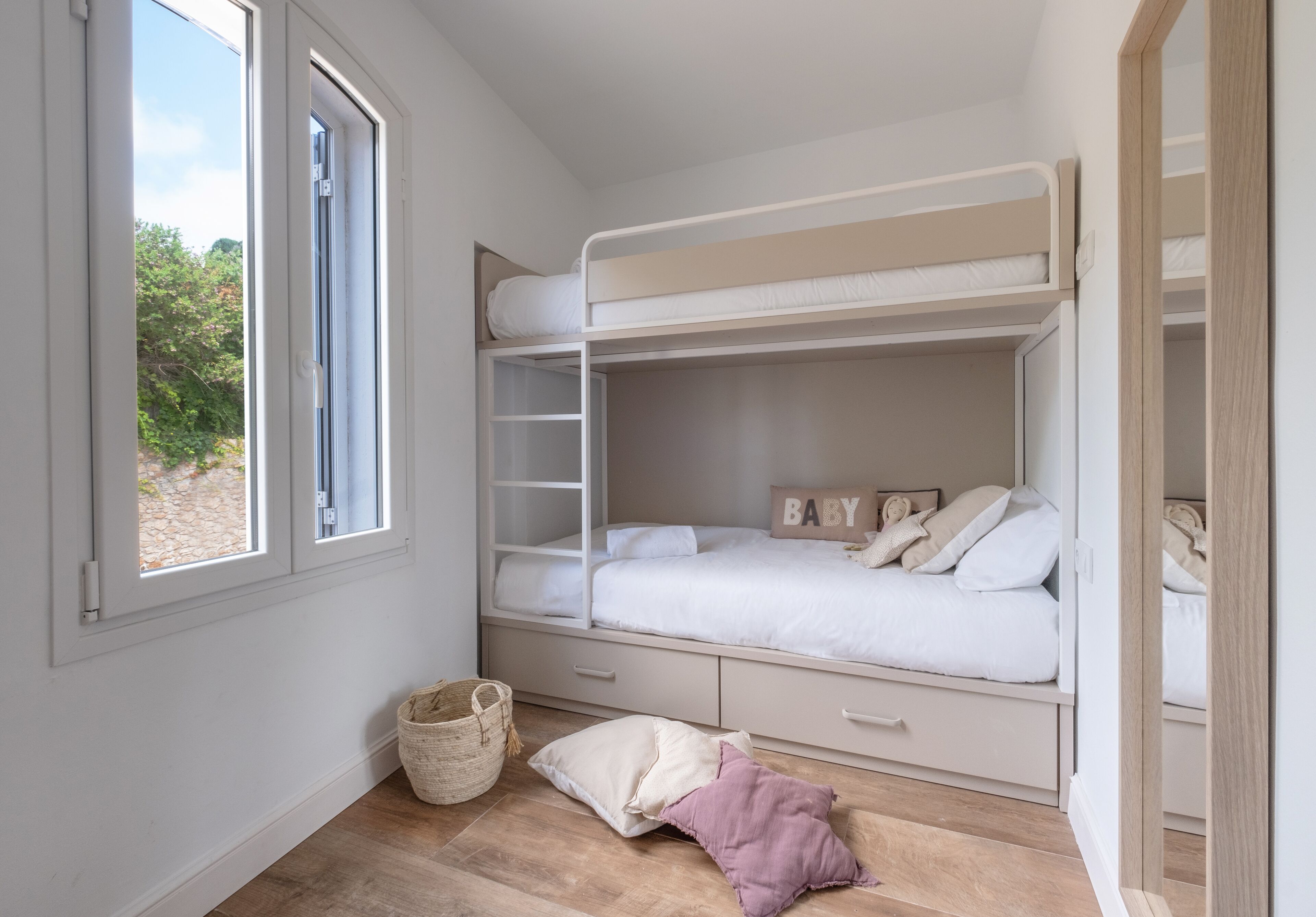 Une chambre avec un lit superposé, une fenêtre, un plancher en bois, un panier et une porte.