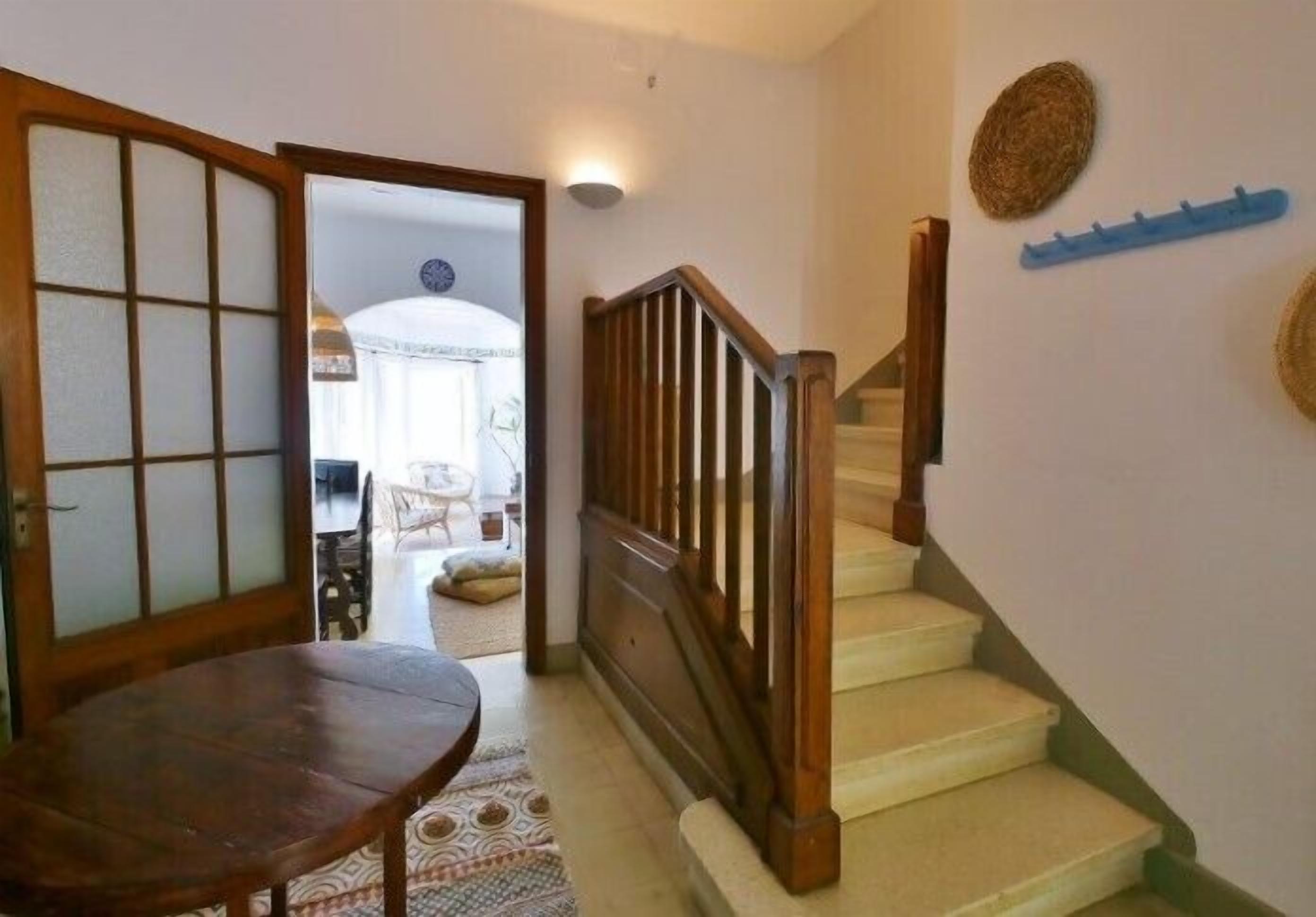 Una escalera con barandillas de madera y un tapete estampado que lleva a un cuarto con una puerta corrediza tradicional japonesa de fusuma.