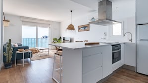 A modern kitchen with a large island, white cabinetry, and a view to the outside. -  Casa Concha Apartamentos (Palafrugell)