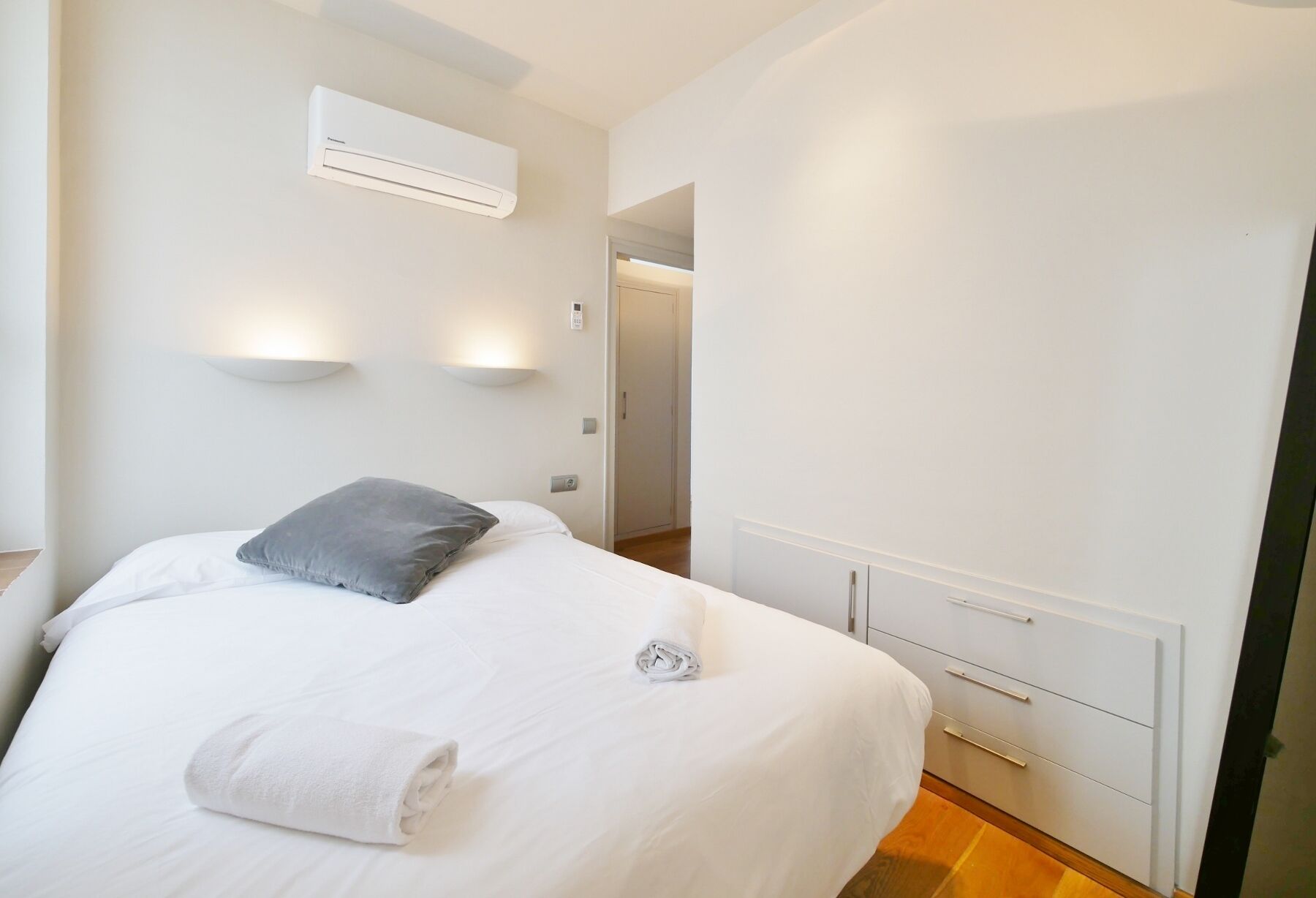Une chambre d’hôtel comprenant un lit, une table de chevet, un climatiseur fixé au mur et une porte donnant sur une autre pièce.
