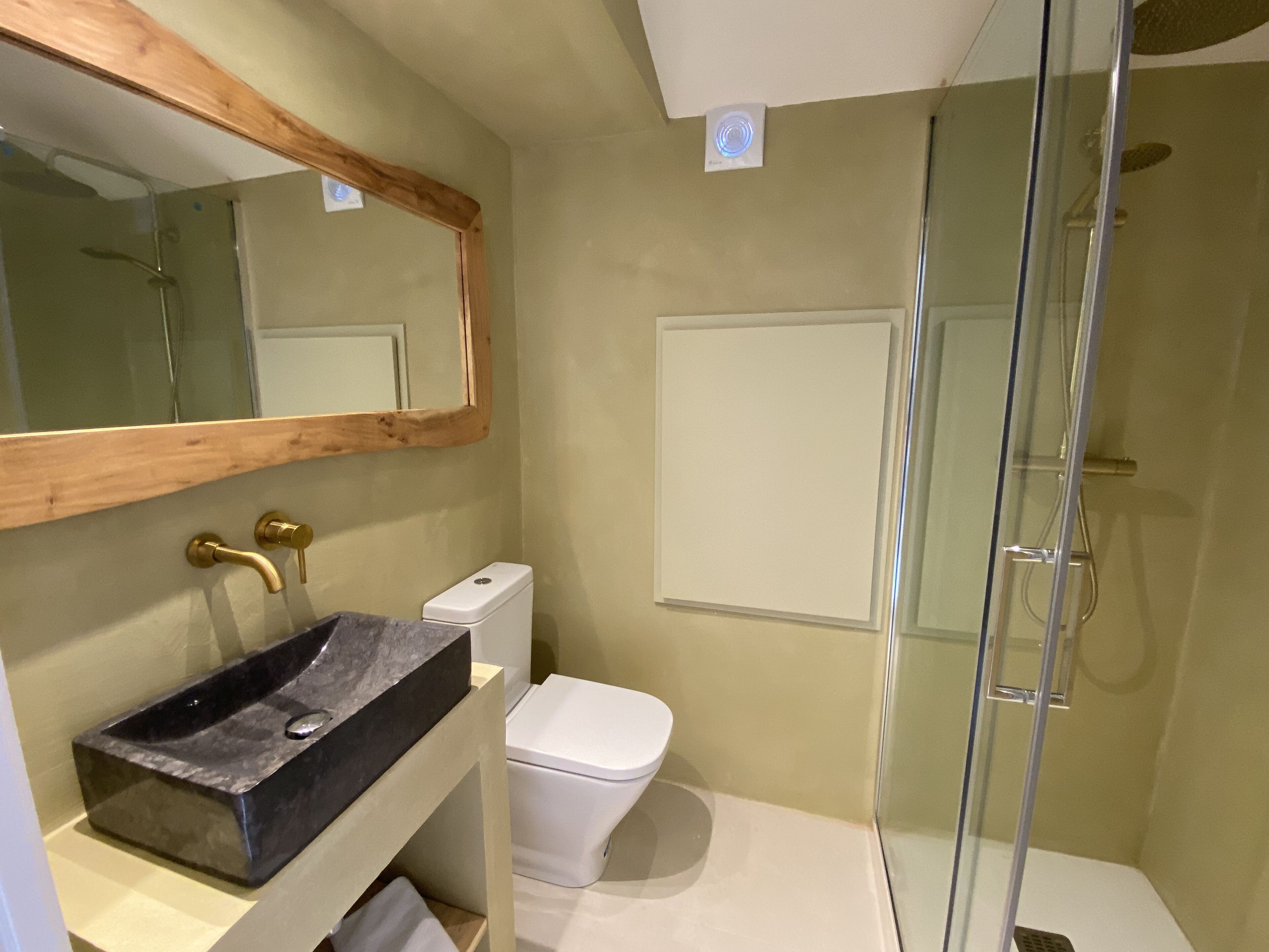 Un bagno con un mobile lavabo in legno, un lavandino nero, un WC bianco e una cabina doccia in vetro.