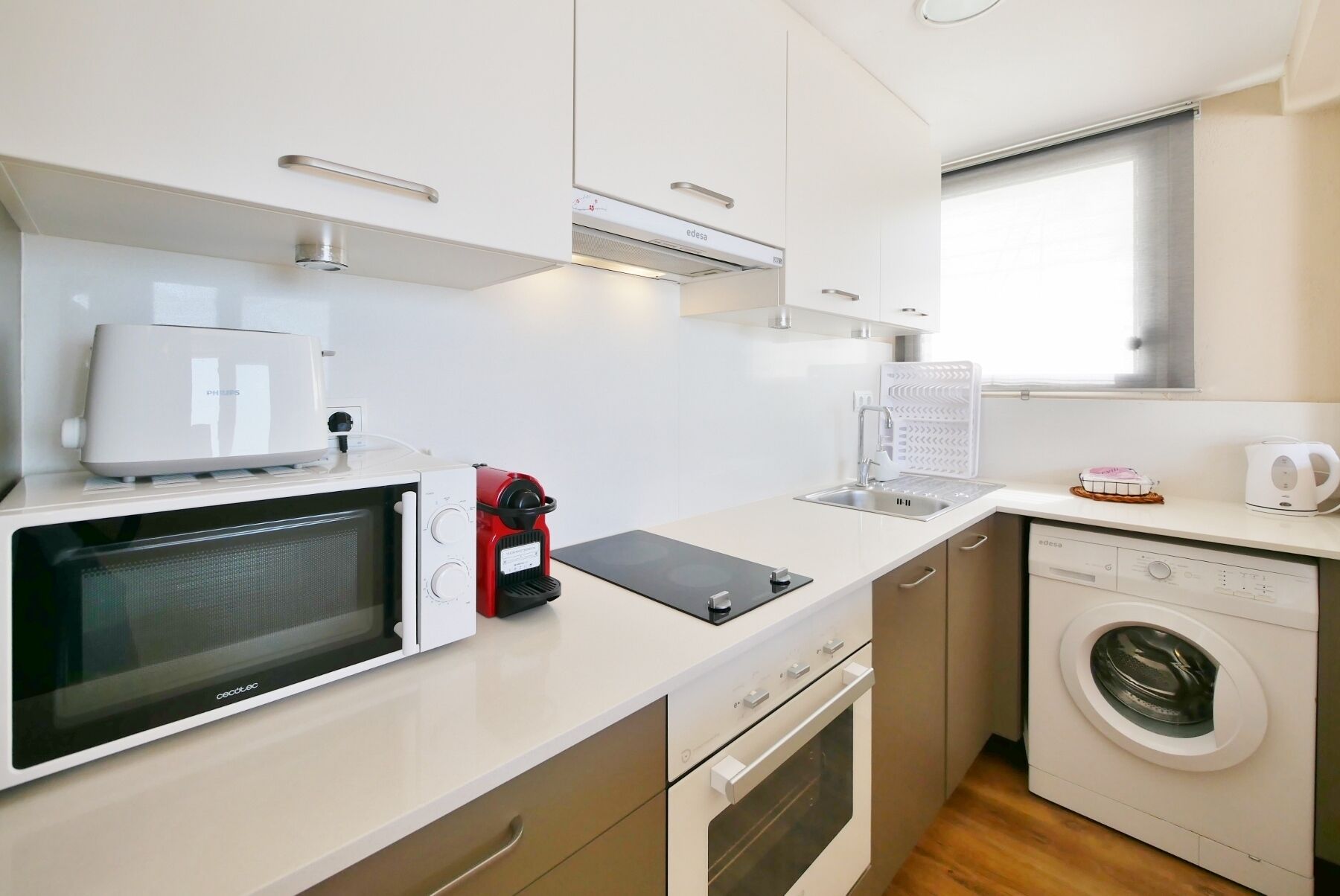 A compact kitchenette with a microwave, toaster, kettle, and a washing machine.