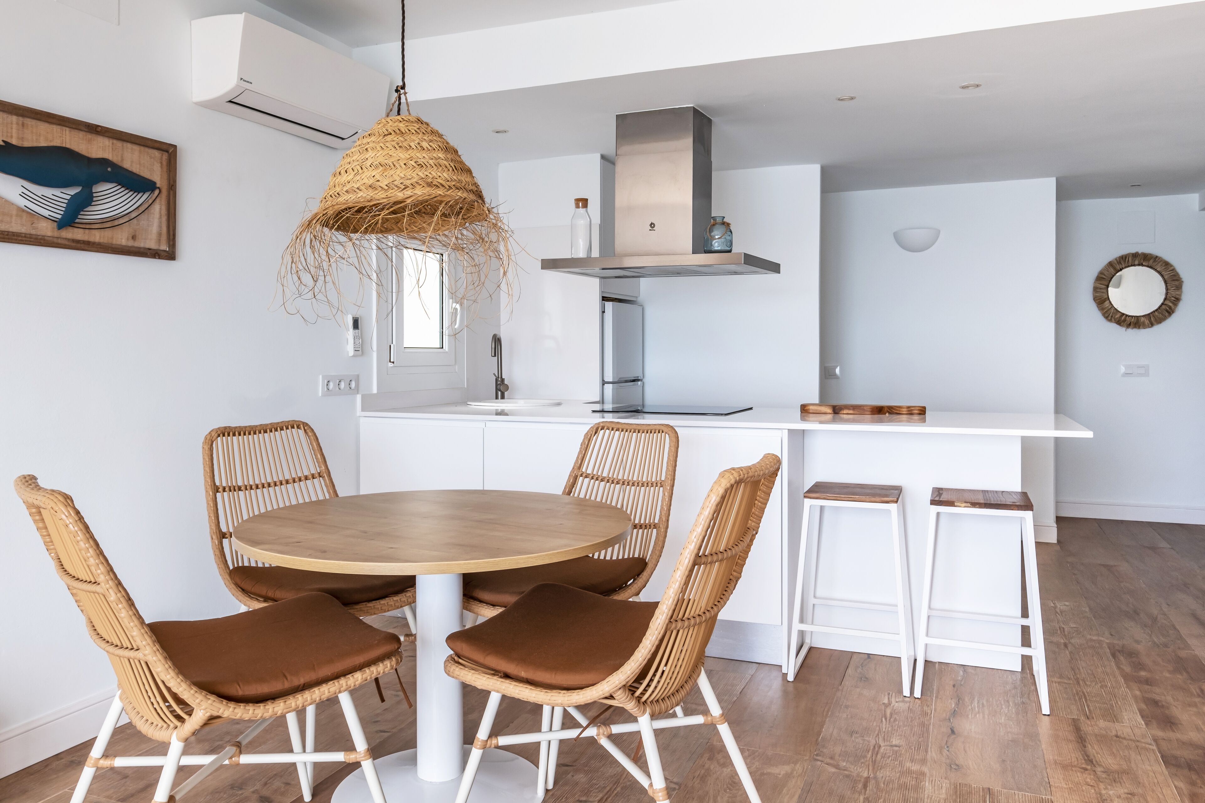 A modern kitchen with a round dining table, wicker chairs, and a hanging light fixture.