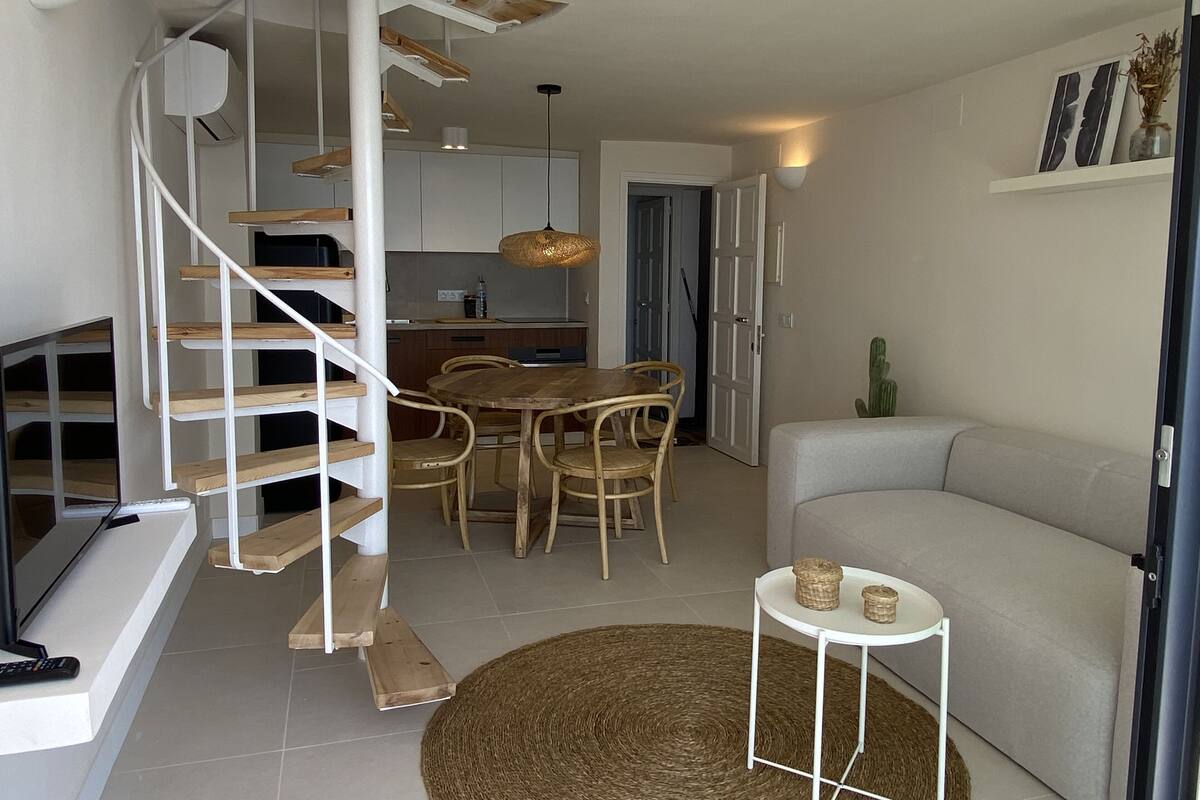 Un espacio de estar moderno con una escalera, comedor y un sofá.