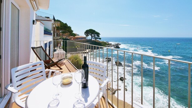 A balcony with a table set for two, overlooking a rocky coastline and the sea. -  Casa Concha Apartamentos (Palafrugell)