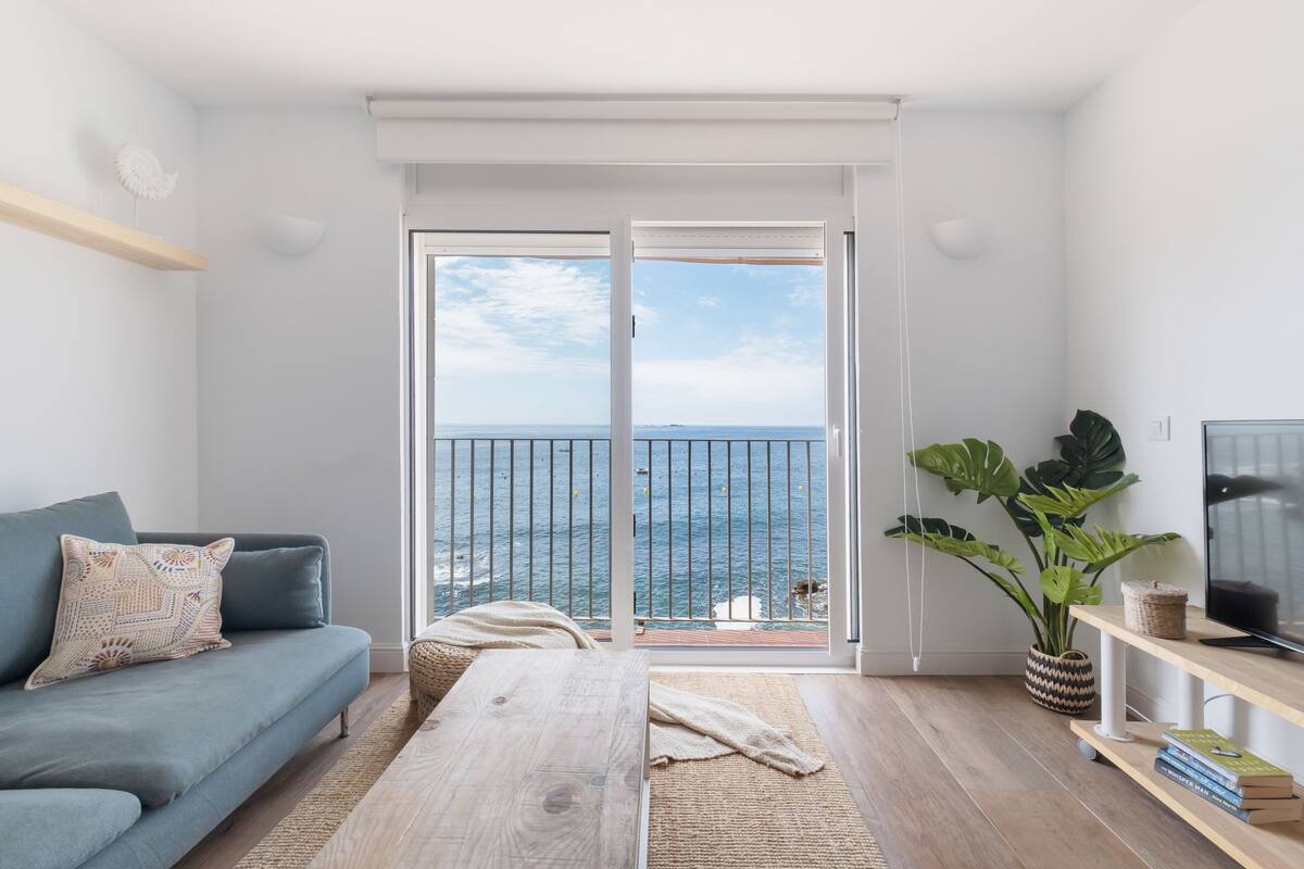 Una sala de estar moderna con sofá, una mesa de centro y un mueble para televisión. Hay un ventanal con vista al mar.