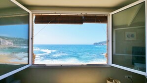 A room with a large window overlooking a beach, a wooden floor, and a small basket on the floor. -  Casa Concha Apartamentos (Palafrugell)