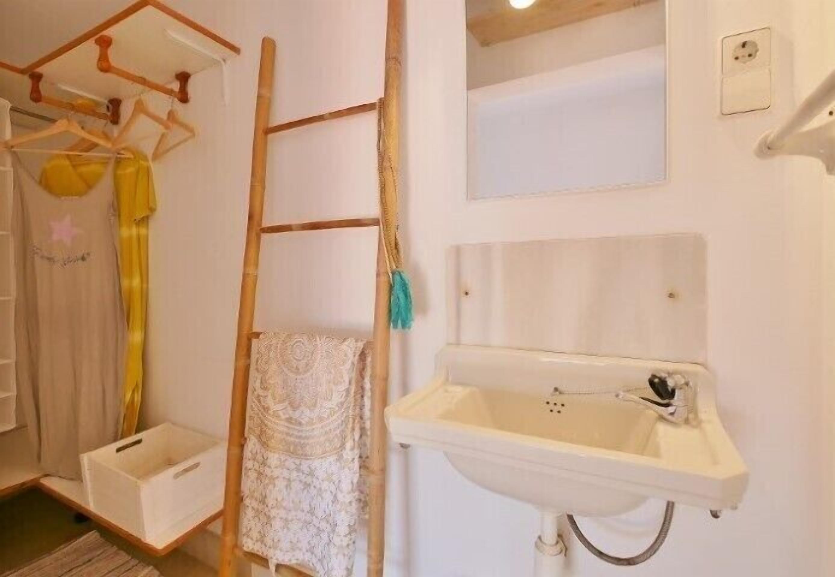 Un baño con un lavabo blanco, una escalera de madera y un espejo.