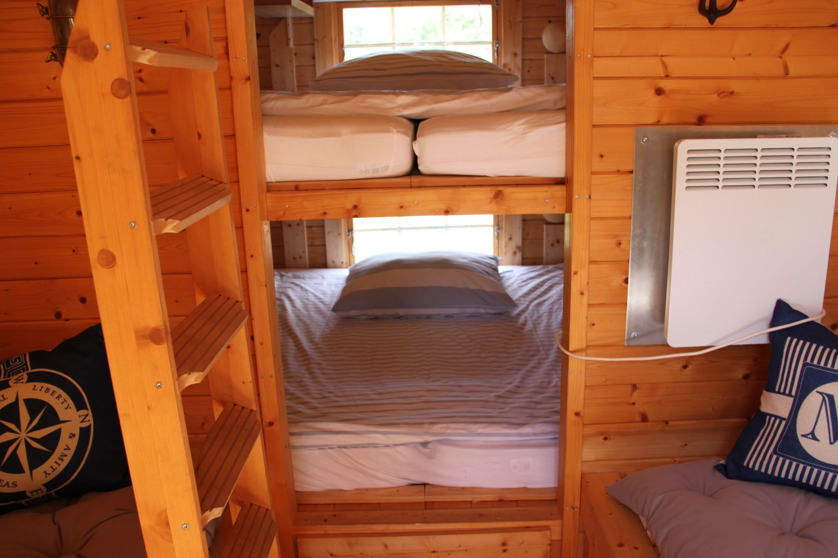 Une cabine équipée de deux lits superposés, d’un chauffage et d’un coussin décoré sur le thème de la boussole.