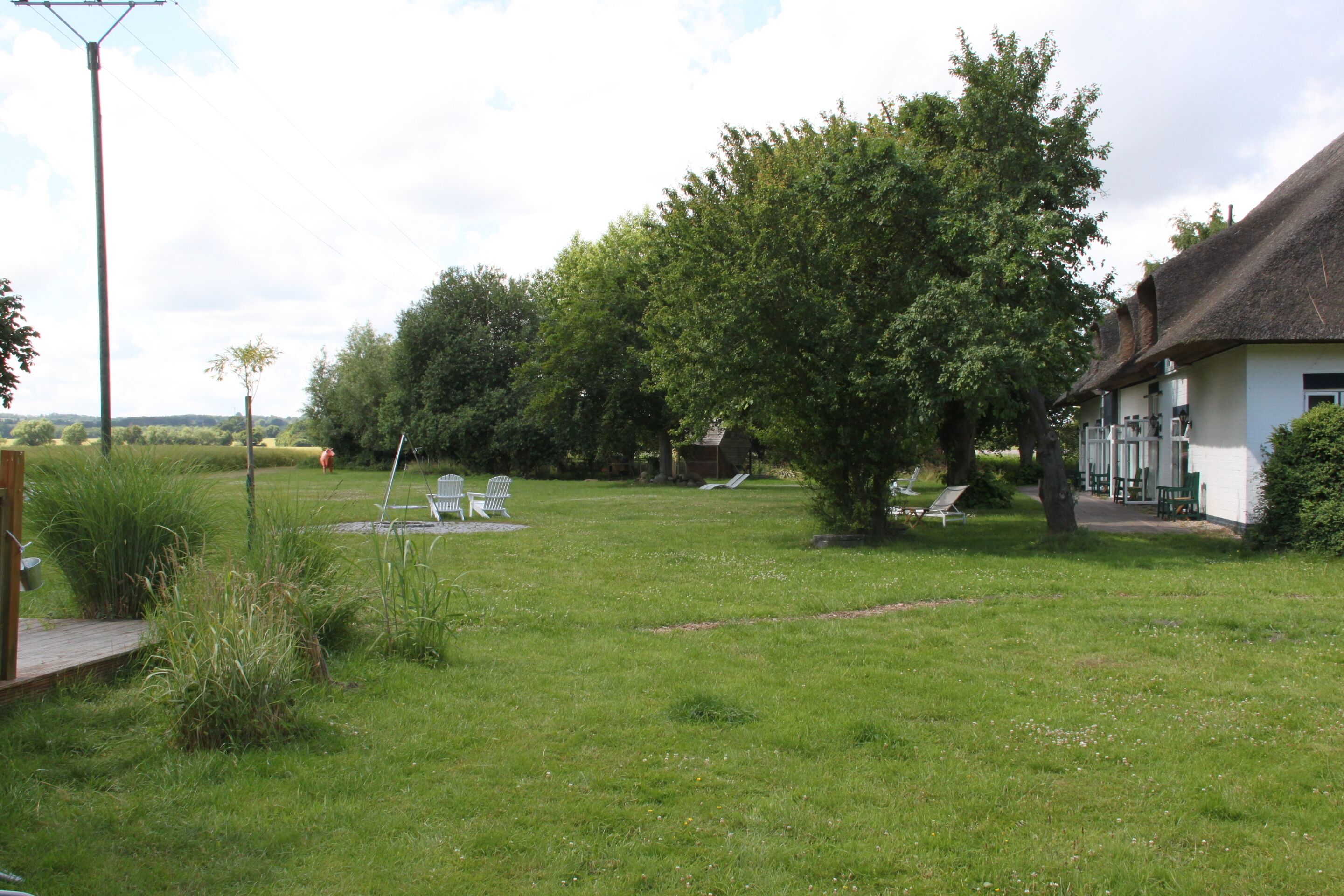 A grassy outdoor area with a thatched-roof building, white chairs, and a wooden deck.