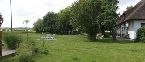 A grassy outdoor area with a thatched-roof building, white chairs, and a wooden deck.