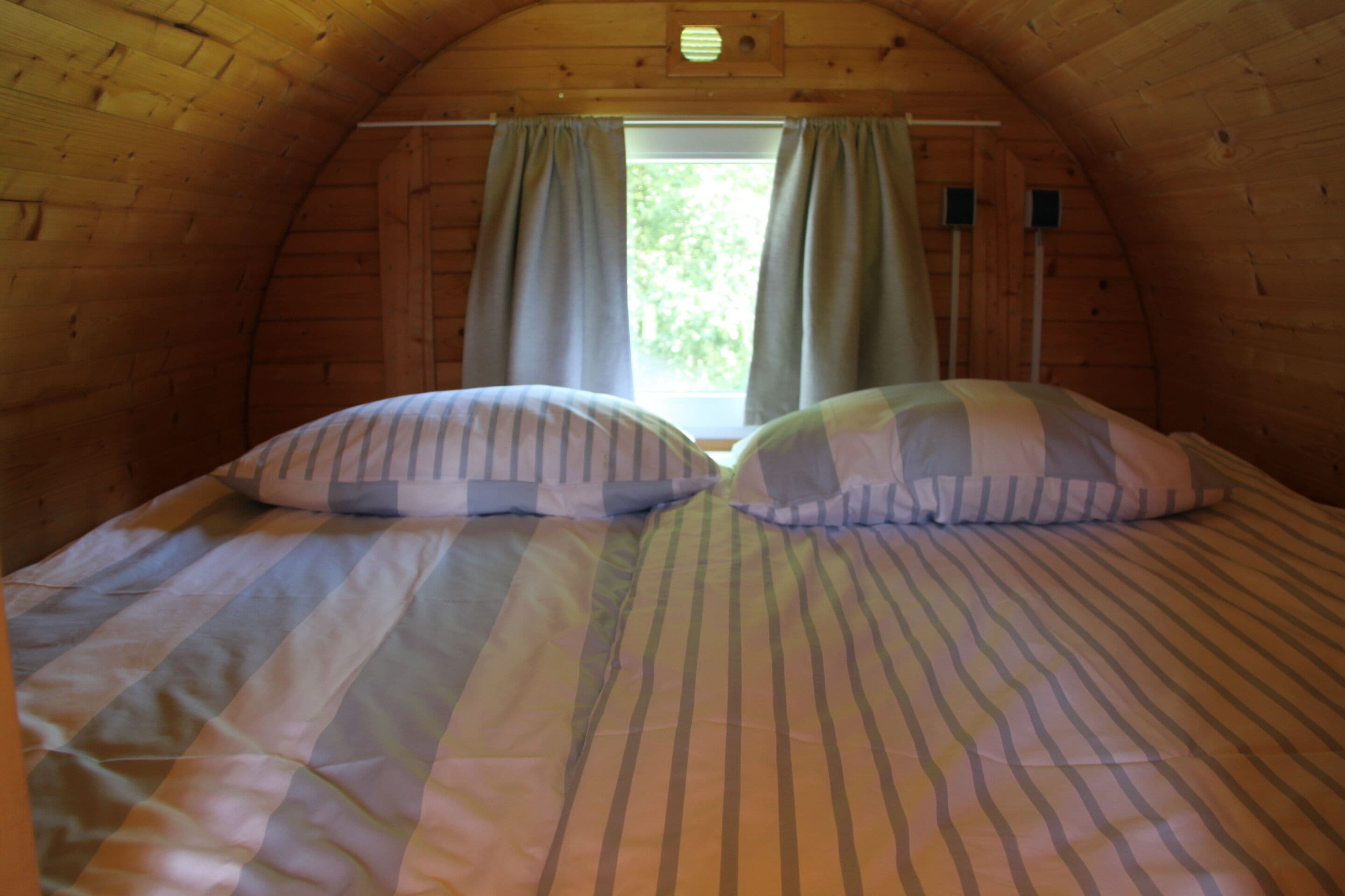 Une chambre mansardée chaleureuse, avec un plafond en pente, une fenêtre avec des rideaux et un lit recouvert d’une literie à rayures.