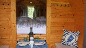 Habitació d'una cabana de fusta acollidora, amb un llit, una taula petita, una ampolla, gots i un plat.
