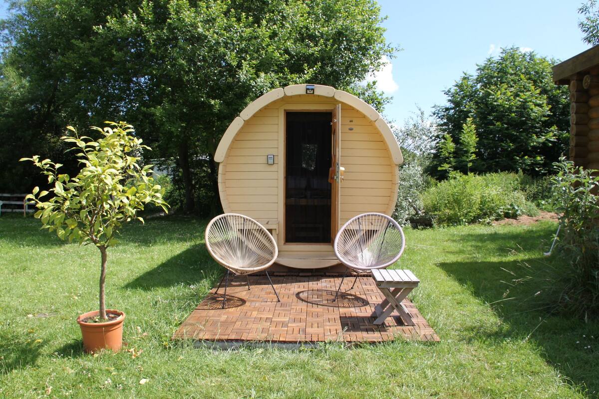 Een klein, rond houten gebouw met een deur, twee stoelen en een tafel ervoor.