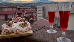 A table with a charcuterie board and two glasses of red beverage, overlooking a cityscape with a mountain in the background.