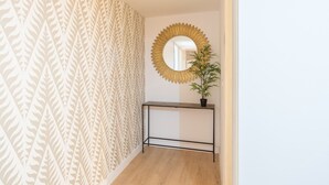 A hallway with patterned wallpaper, a round mirror, a potted plant, and a black console table. - Merced10 3E (Málaga)