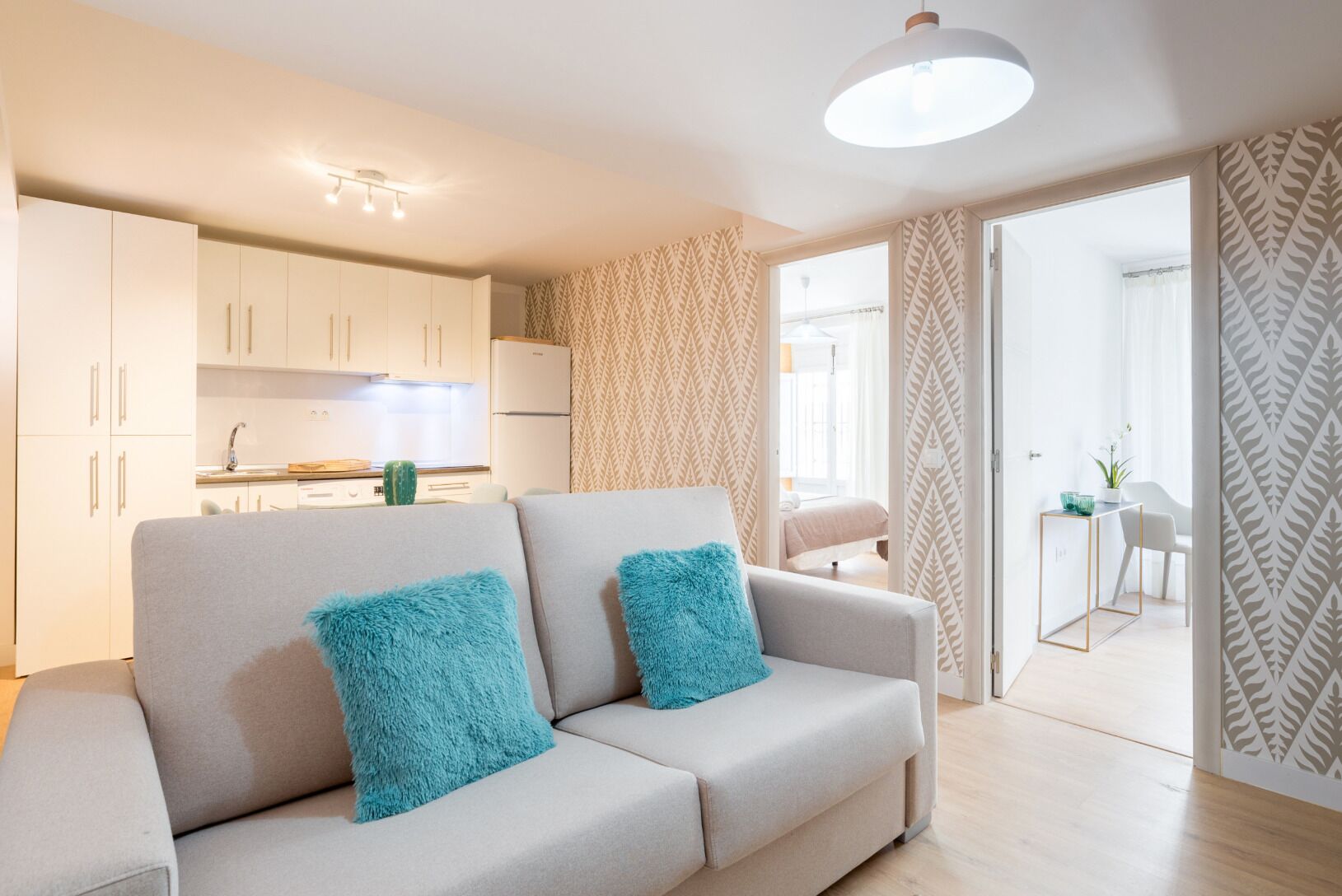 Een moderne woonkamer met een bank, een keuken op de achtergrond en een behang met patroon.