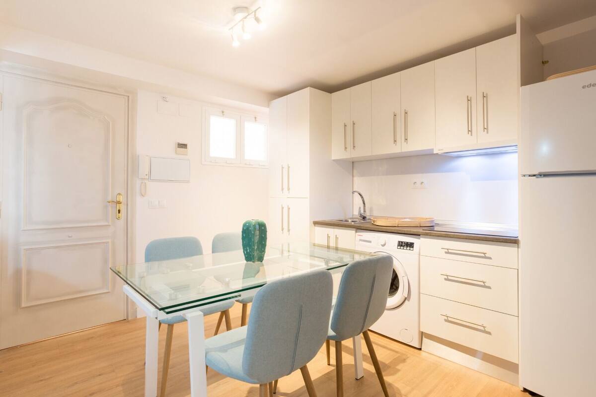 Une cuisine de taille réduite avec des meubles blancs, une table à manger en verre et deux chaises.