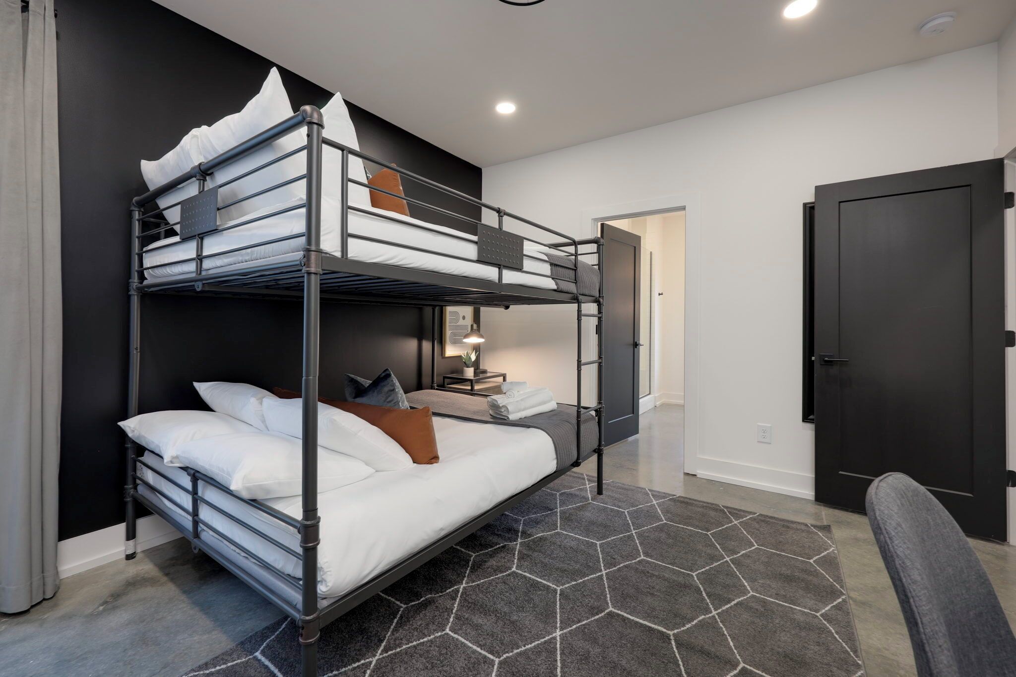 Een slaapkamer met een stapelbed, bureau en stoel, een deur en een kamerkleed met patroon.