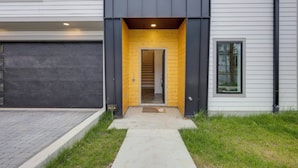 Ein modernes Haus mit dunkler Fassade, einer Holztür und einer sichtbaren Treppe, die ins Innere führt.