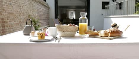 Desayuno en un balcón con pared de ladrillo, mesa blanca y vista a un edificio con ventana y puerta.