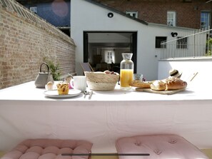 A breakfast setup on a balcony with a brick wall, a white table, and a view of a building with a window and a door. - La Maison Harmony holidays near Cabourg 2 à 12 p (Beuvron-en-Auge)