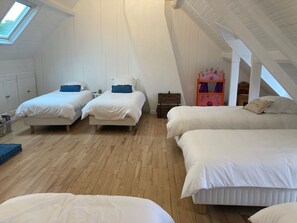 A high-ceilinged room with three beds, wooden flooring, and a skylight.