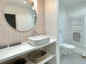 A modern bathroom with a white sink, mirror, and toilet. There are two baskets under the sink and a towel rack with a towel. - La Maison Harmony holidays near Cabourg 2 à 12 p (Beuvron-en-Auge)