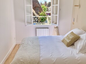 A bedroom with a large bed, a window with a view of buildings, and a radiator.