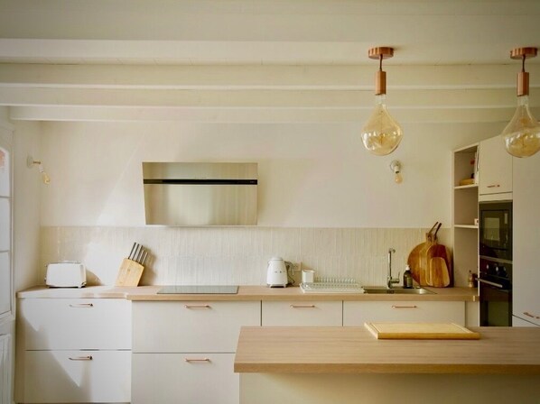 A modern kitchen with white cabinetry, a wooden countertop, and pendant lighting.