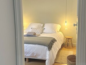 A bedroom with a bed, pillows, a bedside table, and a hanging light fixture.