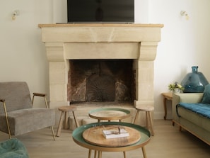 A living room with a stone fireplace, two round glass tables, a sofa, and a television mounted above the fireplace.