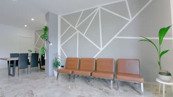 Un'area d'attesa dal design moderno, con una disposizione di sedute che include poltrone nere e marroni, una parete bianca con motivi geometrici e un pavimento in marmo.