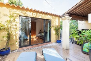 A patio with a sliding glass door leading to an interior space, a wooden deck, and potted plants. - Small warm house near the sea (La Garde)