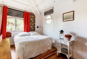 A bedroom with a bed, a bedside table with a lamp, a window with curtains, and a picture on the wall. - Small warm house near the sea (La Garde)