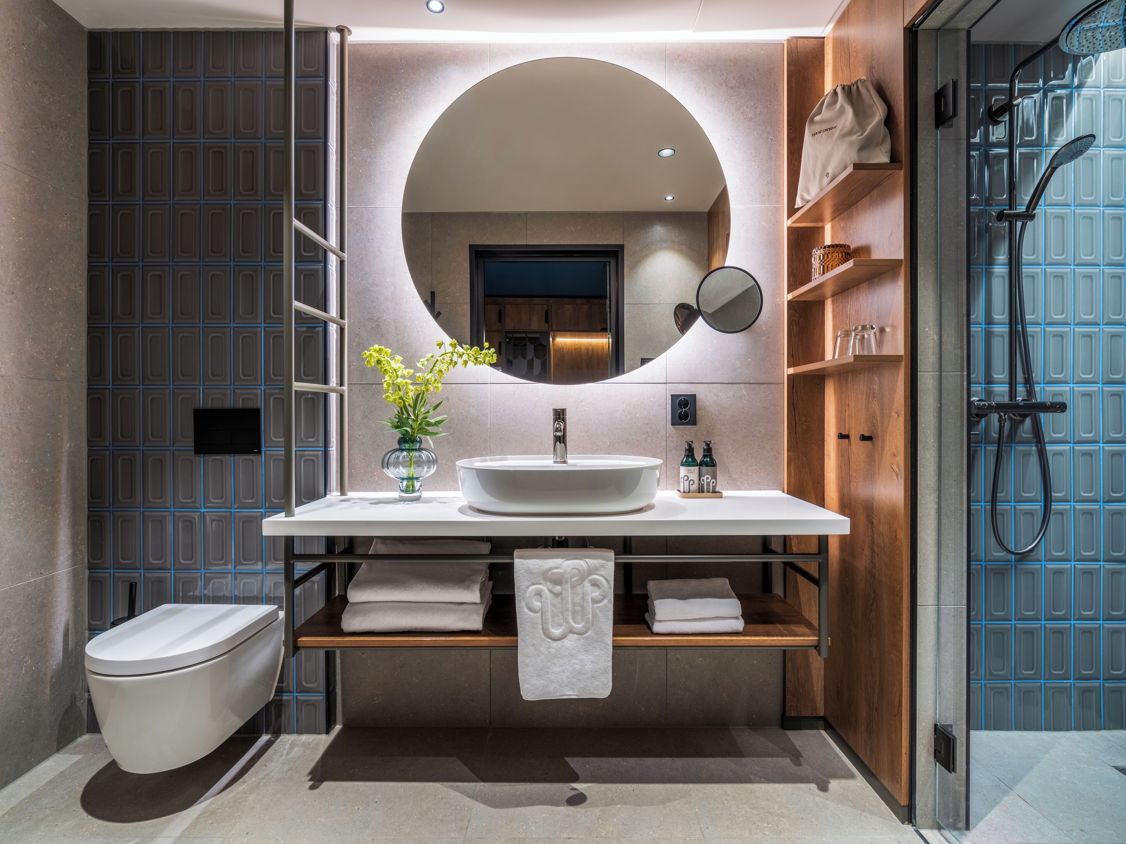 A modern bathroom with a large round mirror, a white sink, and a shower area.