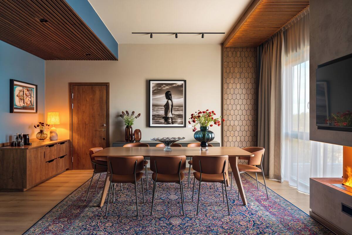 A modern dining area with a wooden table, six chairs, a patterned rug, and a large framed artwork on the wall.
