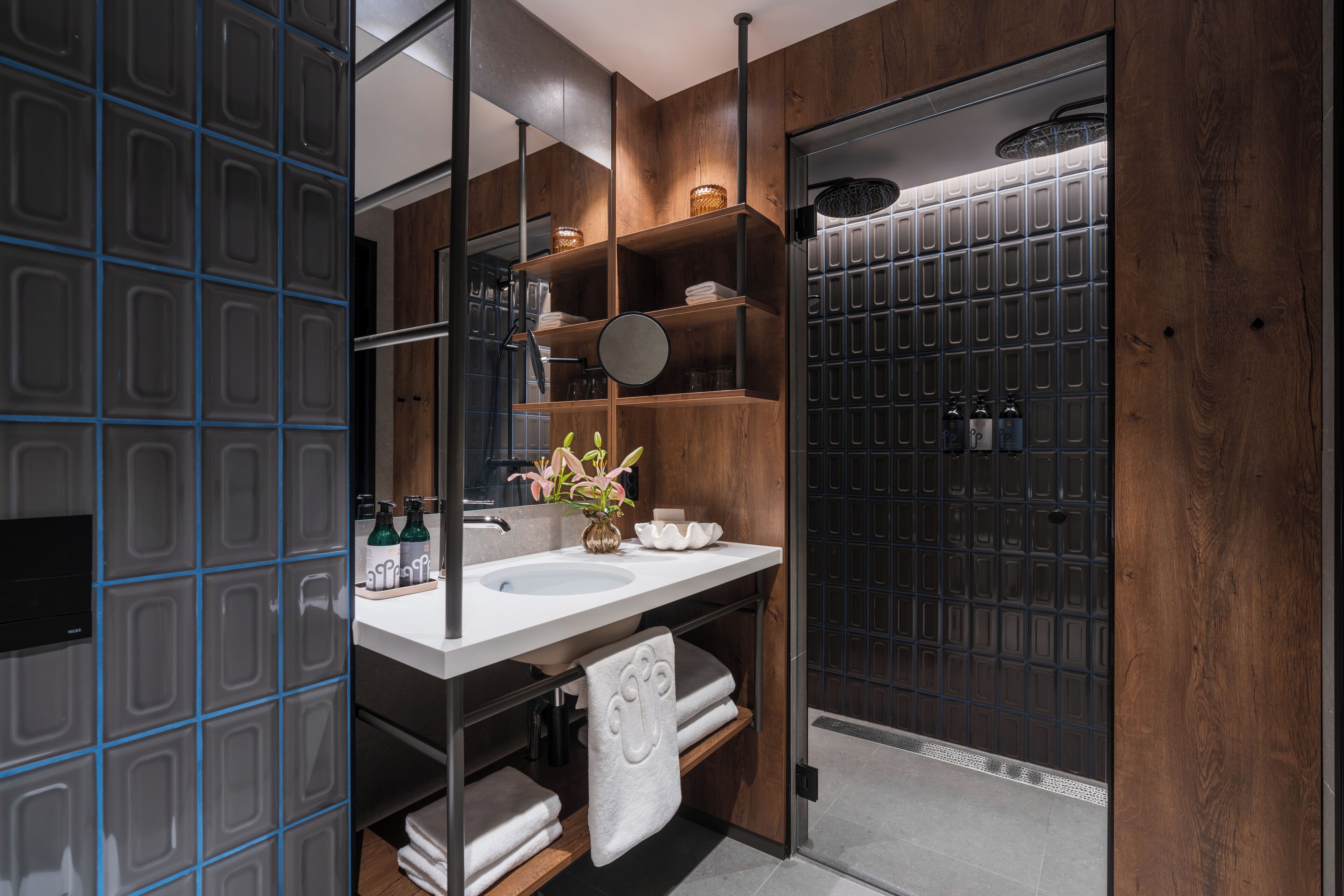 Un baño moderno con un espejo grande, estantes de madera, un lavamanos blanco y una zona de ducha.