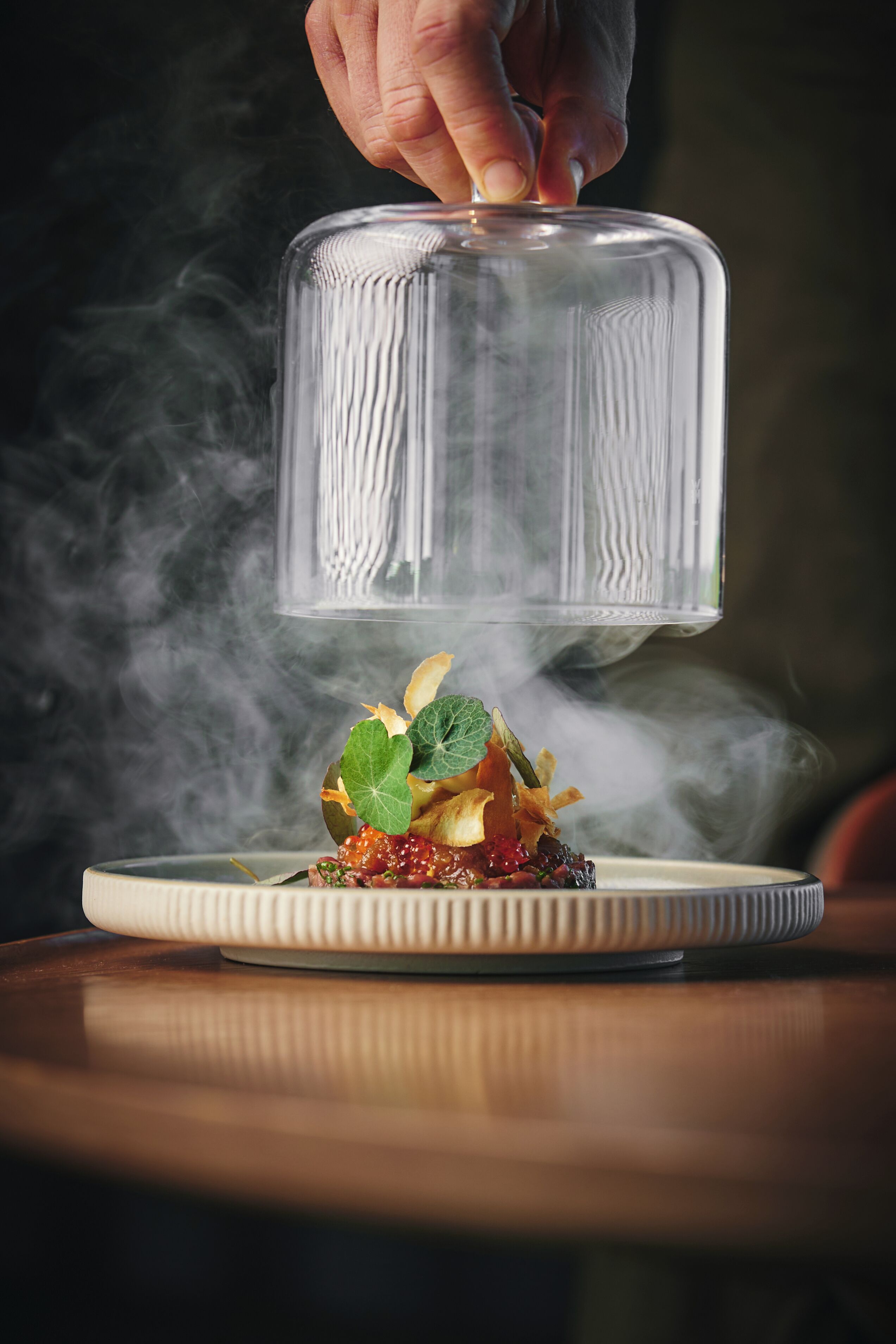 Una mano colocando una tapa sobre un plato con comida y humo.