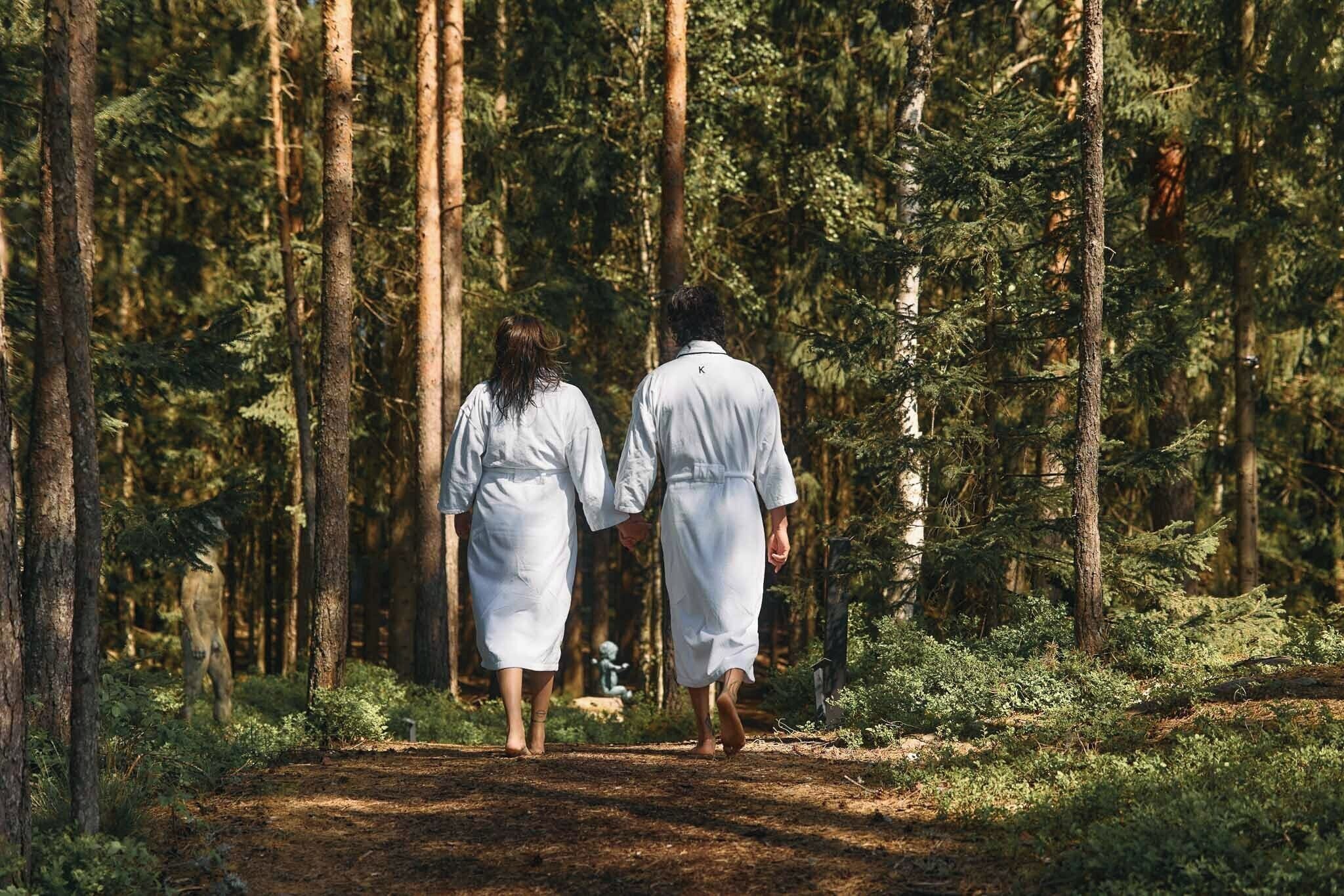 Two people walking away from the camera in a forested area.