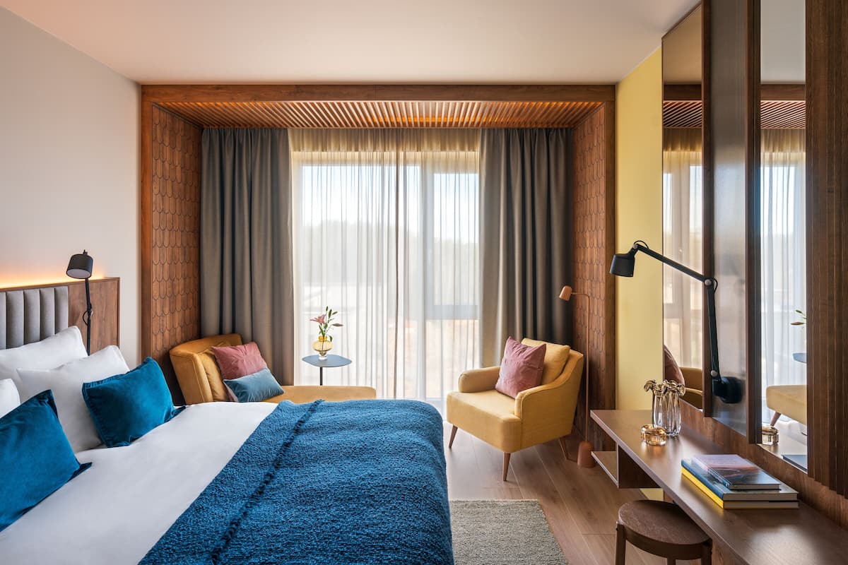 A hotel room with a bed, a desk, a chair, a lamp, and a large mirror.