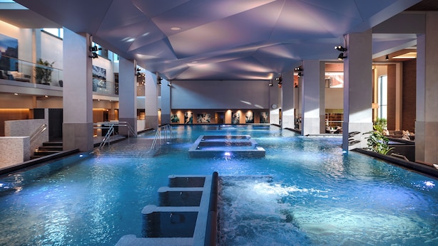 A large indoor swimming pool with multiple lanes, a glass balustrade, and a modern ceiling design. - The Well Spa & Hotel (Nordre Follo)