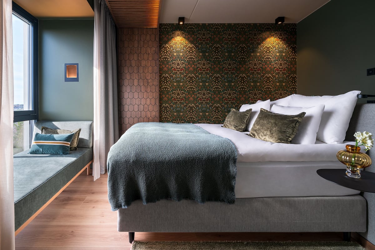 A modern bedroom with a bed, bedside table, and a view of the city.