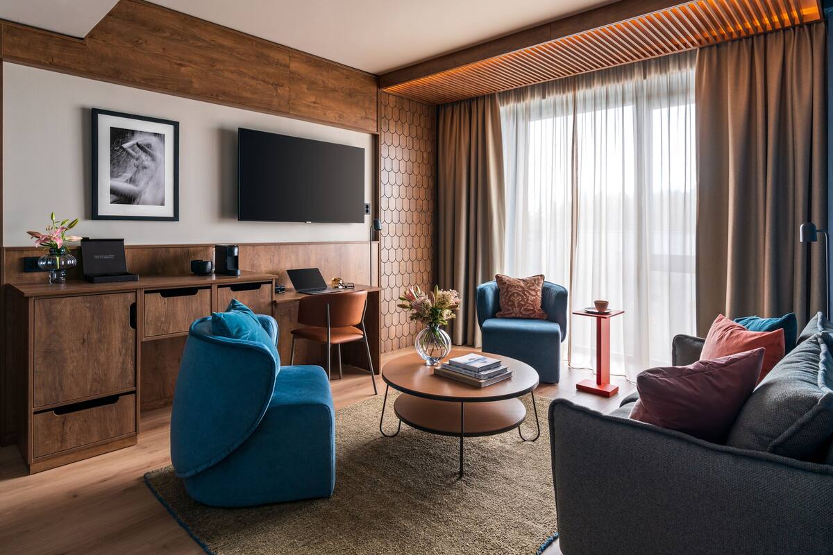 A modern living room with a wooden accent wall, a flat-screen TV, a blue sofa, a coffee table with books, and a desk with a laptop.